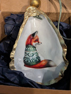Decorative shell with a painted fox wearing a sweater inside, on a dark fabric background.