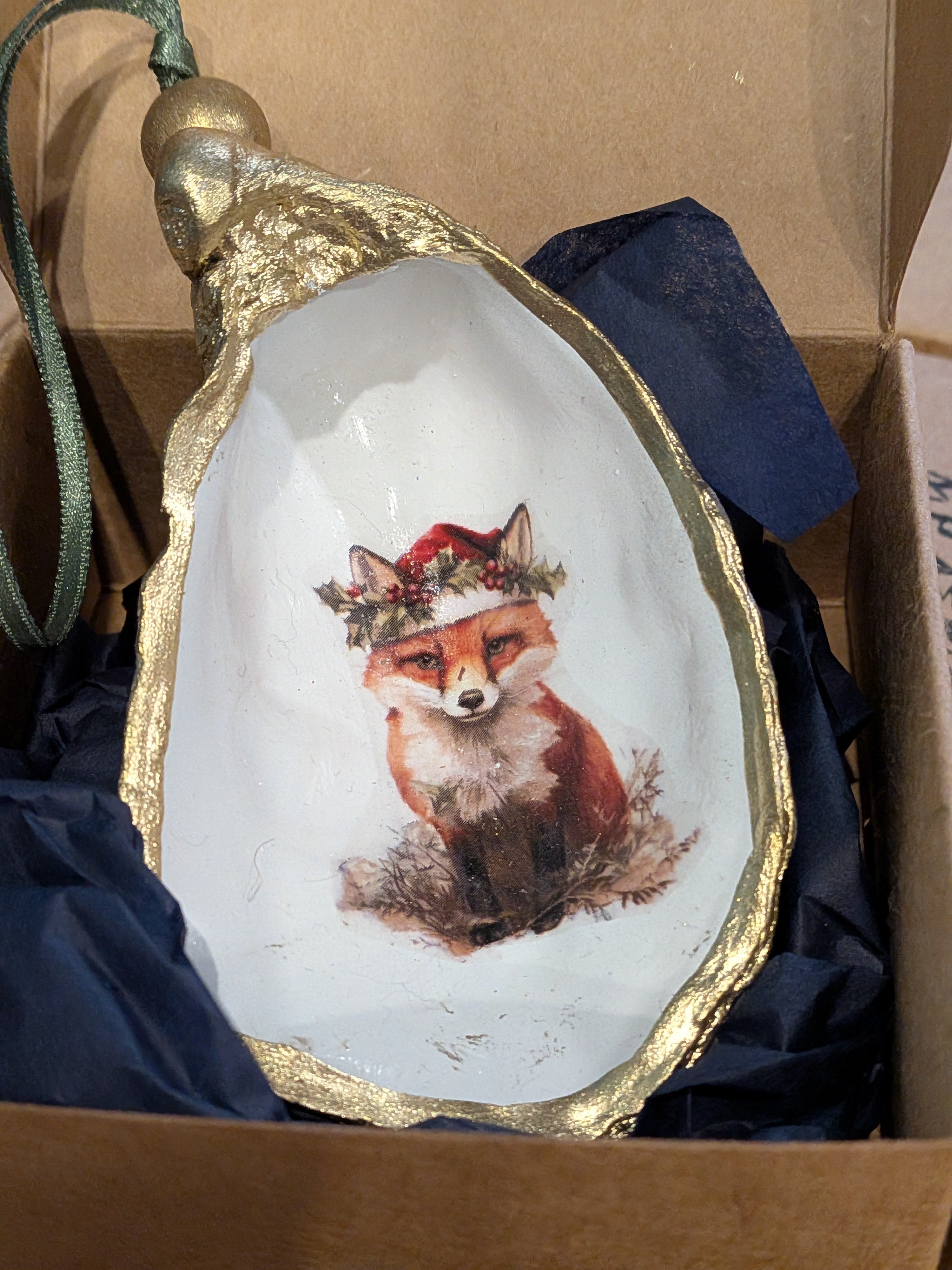 Decorative plate with a fox illustration wearing a wreath, set against a cardboard box background.