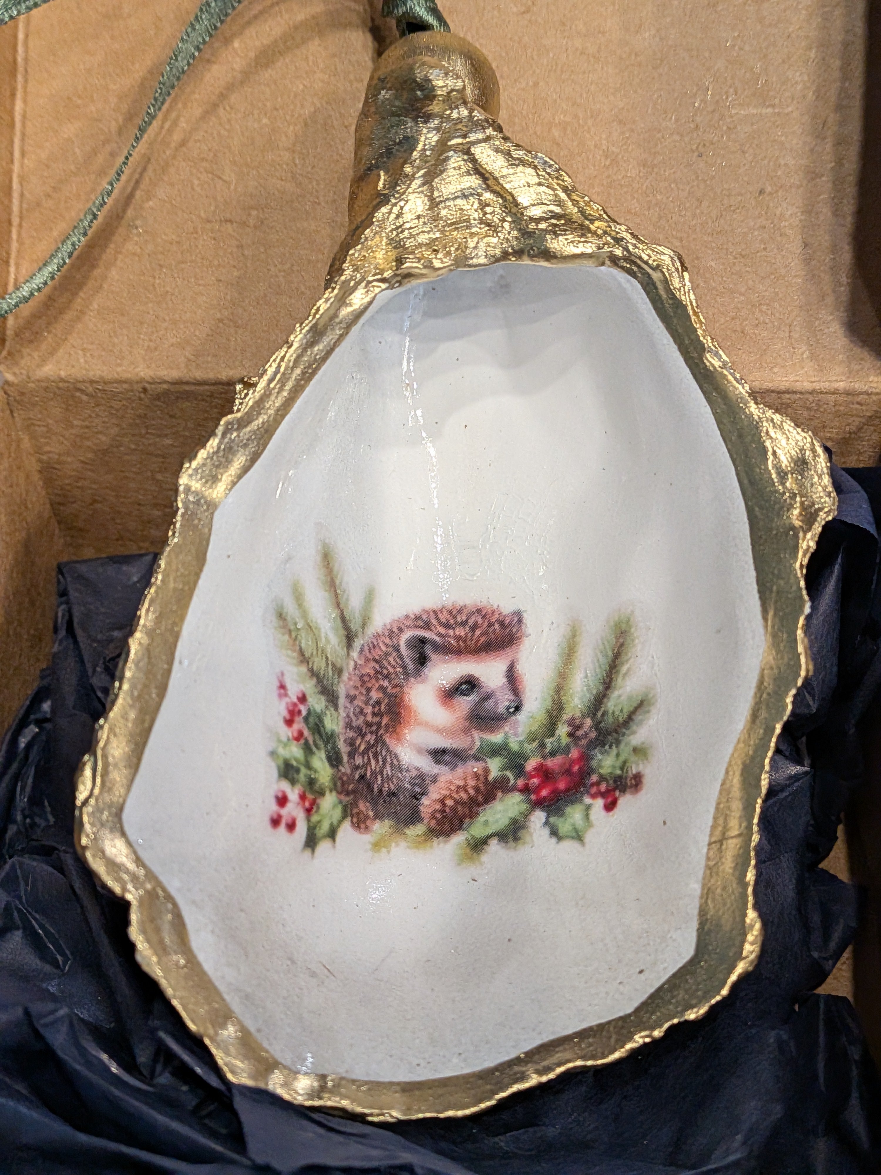 Decorative shell with a hedgehog design on a gold rim, placed on a dark fabric background.
