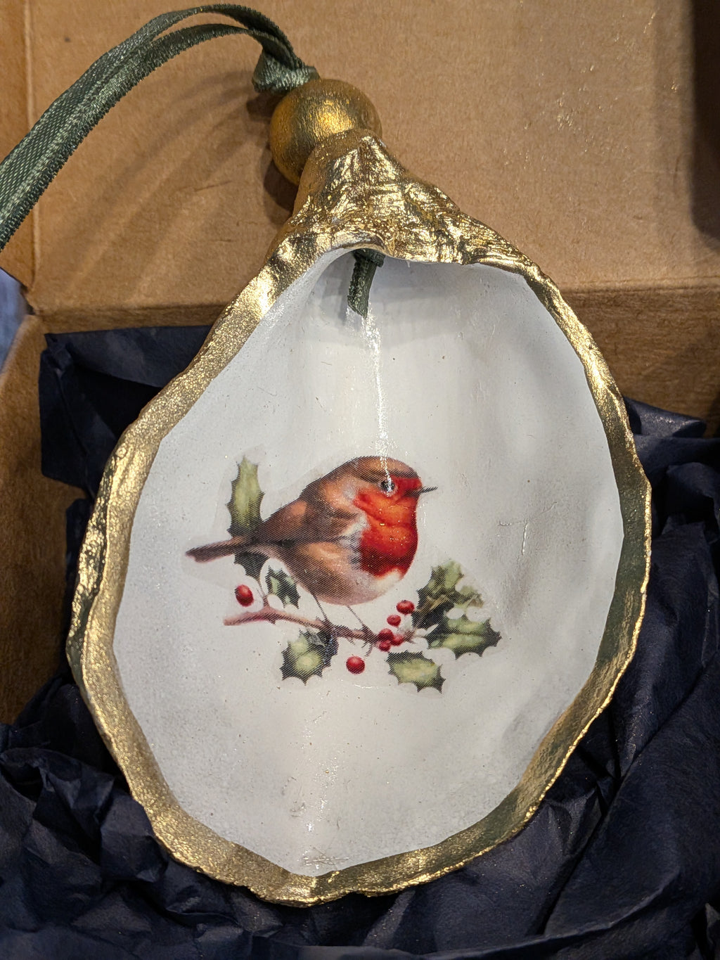 Decorative shell ornament with a robin design on a gold rim, against a dark fabric background.